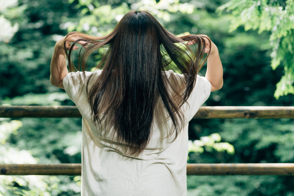 自然の中で長い髪を持ち上げる女性の後ろ姿